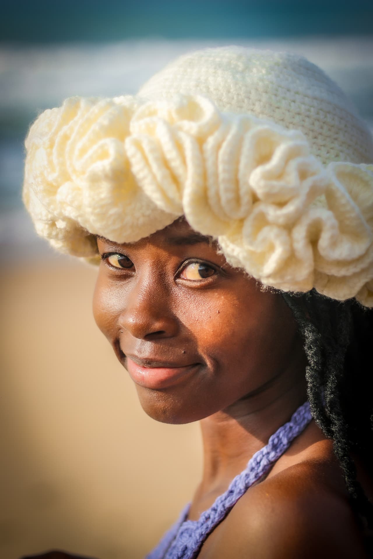 Close portrait of a model in a textured cream crochet hat on the beach