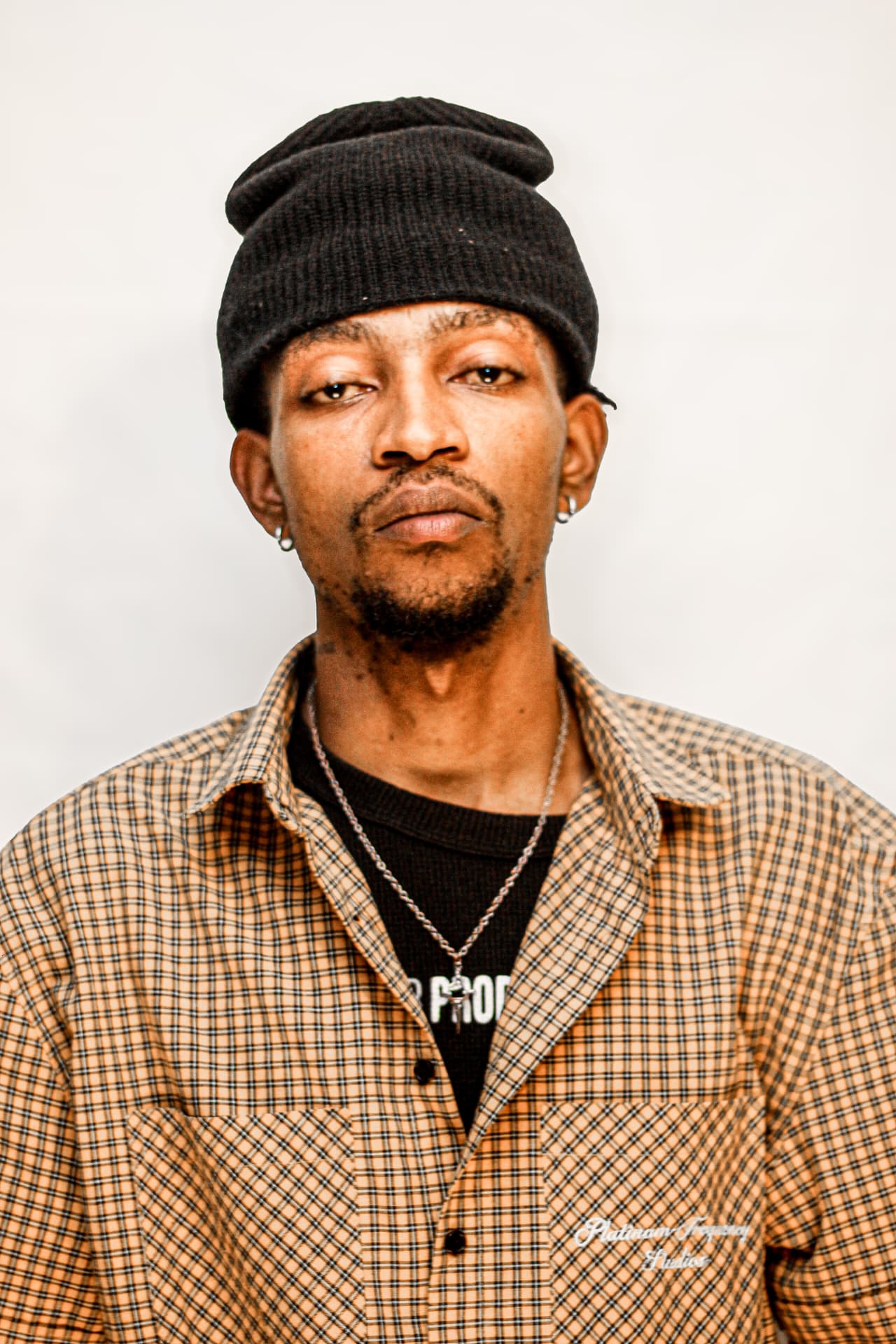 Head and shoulders studio portrait of a man in a beanie and checked overshirt