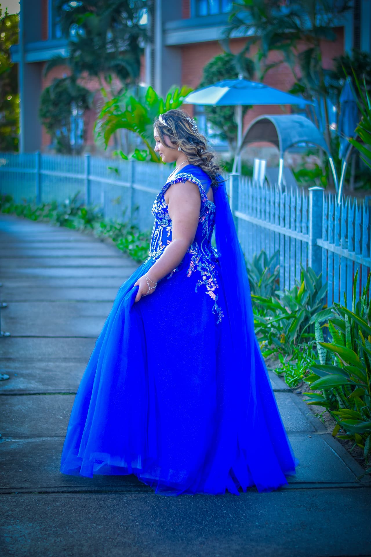 Debutante turning to camera in a sapphire ball gown on a garden walkway