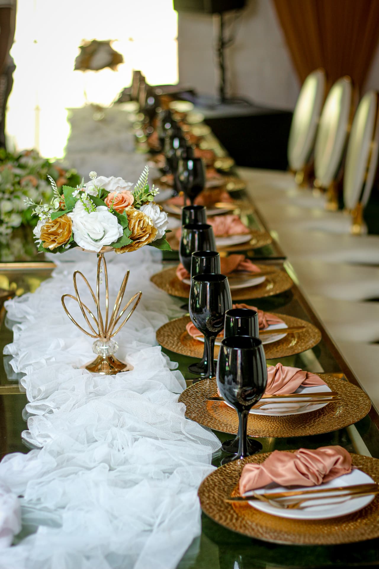 Long mirrored reception table dressed with tulle runner, gold chargers and blush napkins