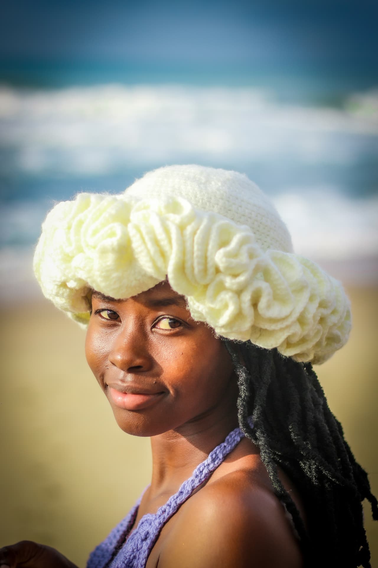 Portrait of a model in a cream crochet hat and lilac crochet top by the sea