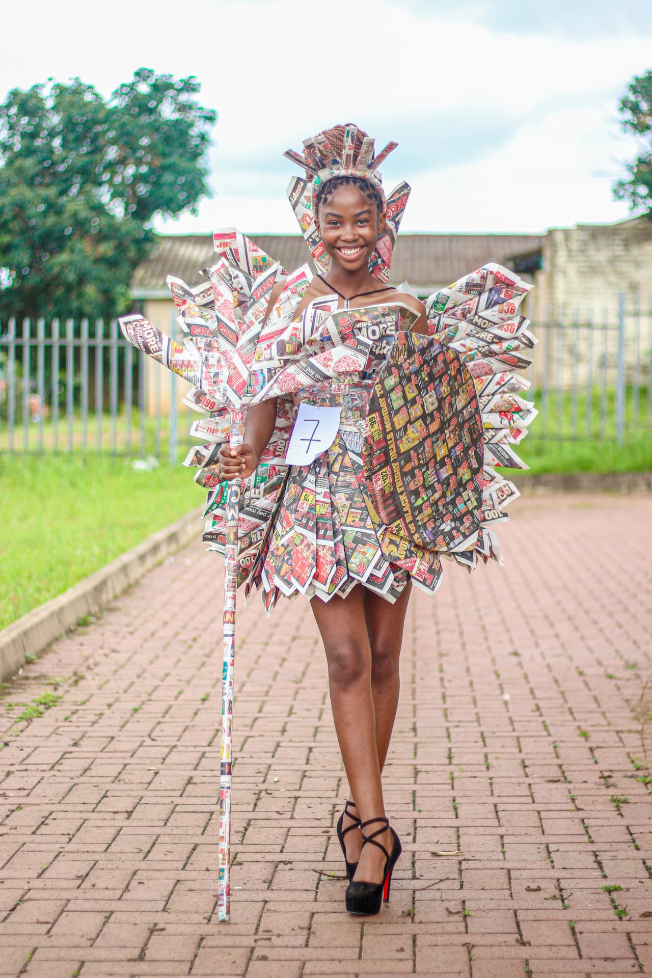 Young contestant in a couture outfit built from printed newspaper wings and headpiece