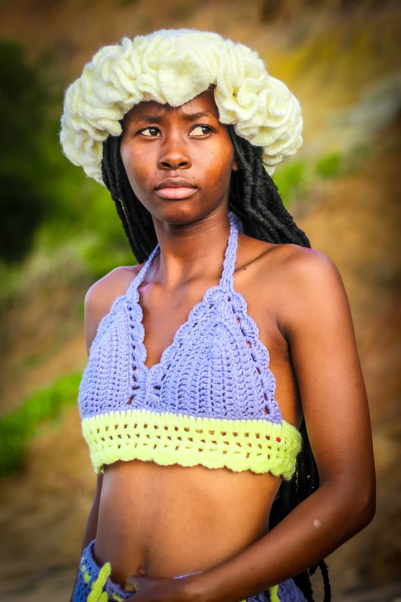 Model in handmade lilac and lime crochet top photographed against dune grass