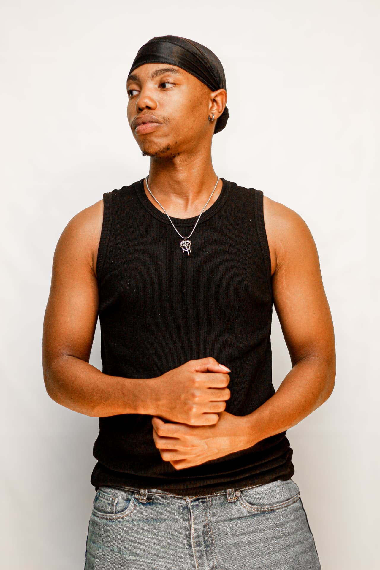 Studio portrait of a young man in a black vest and durag looking off camera