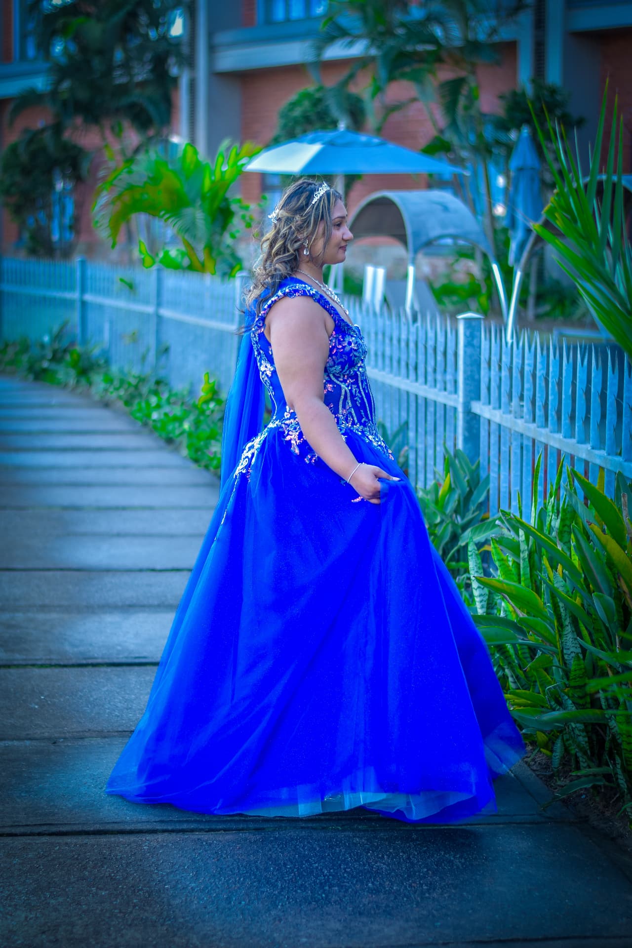 Matric ball debutante in a sapphire tulle gown walking a garden path at dusk