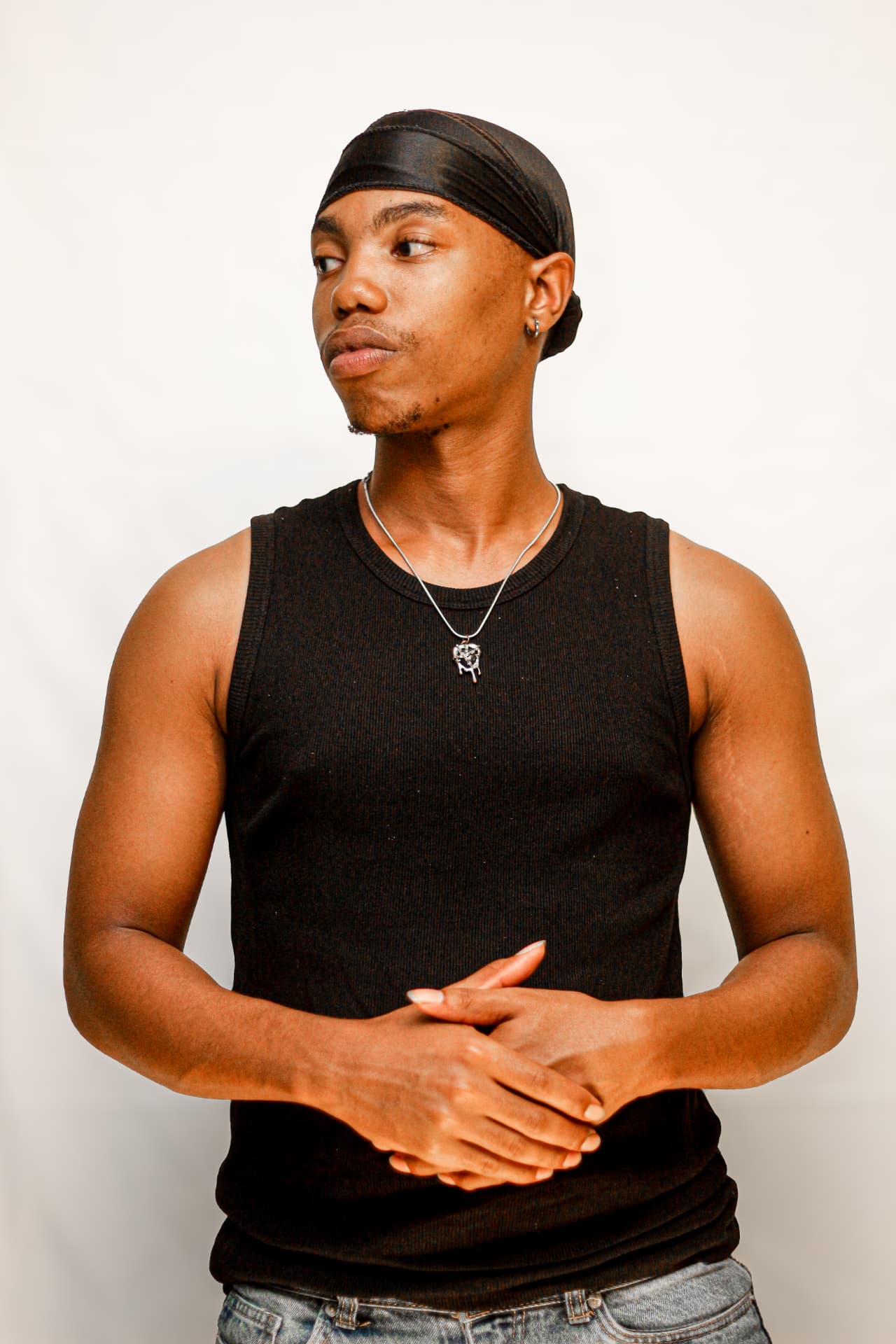 Calm studio portrait of a young man in a black vest with hands clasped